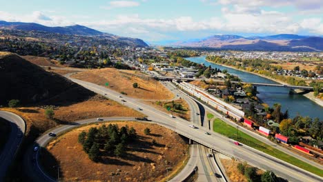 normal-speed-dolly-in-drone-shot-of-Kamloops-BC-Canada-with-Bridges,-the-Highway-1-and-Yellowhead-Highway-5-on-a-sunny-day-in-the-desert-city-with-cars,semi-trucks-and-trains-driving-in-the-foreground