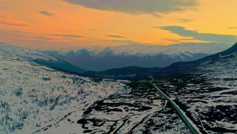 Luftdrohne,-Die-Sich-Rückwärts-über-Eine-Schneebedeckte-Landstraße-Auf-Einem-Bergplateau-Bewegt,-Umgeben-Von-Einer-Wunderschönen-Norwegischen-Bergkette-In-Der-Ferne