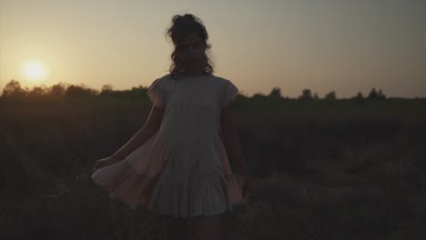 Slow-motion-handheld-panning-shot-of-a-young-pretty-woman-dressed-in-a-dress-during-a-beautiful-sunset-in-nature