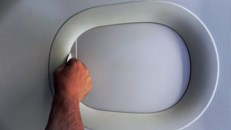 Passenger-hand-closing-aircraft-window-blind-from-which-airplane-wing-and-clouds-can-be-seen