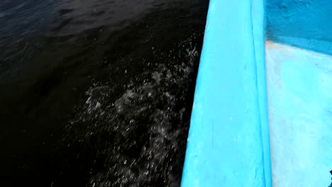 Detail-shot-of-the-side-of-a-blue-fiber-motorboat-navigating-as-waves-splash
