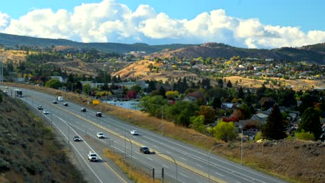 pan-right-shot-hyperlapse-of-Highway-1-in-Kamloops-BC-Canada-,-with-cars-and-semi-trucks-driving,-the-city-in-the-background-in-a-desert-environment-on-a-cloudy-day