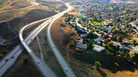 normal-speed-dolly-in-drone-shot-of-Highway-1-in-Kamloops-BC-Canada-,-with-cars-and-trucks-driving-on-the-road,-the-city-in-the-background-in-a-desert-environment-on-a-sunny-day