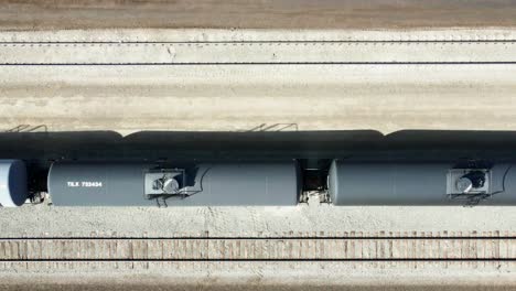 bird's-eye-view-dolly-right-drone-shot-flying-over-railroad-station-in-a-desert-environment-on-a-sunny-day-over-black-tank-trains