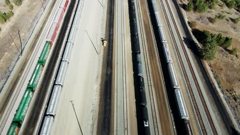 bird's-eye-view-dolly-forward-drone-shot-flying-over-railroad-station-in-a-desert-environment-on-a-sunny-day-next-to-a-highway-and-a-river