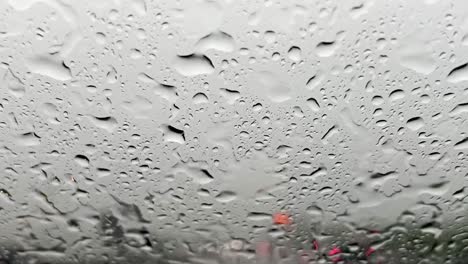 Heavy-rain-falling-on-windscreen-and-red-blurred-lights-of-car-traffic-in-background-with-wiper-cleaning-windshield-from-raindrops