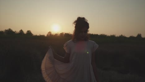 Slow-motion-static-shot-of-a-young-pretty-indian-woman-standing-on-a-field-in-nature-during-a-beautiful-sunset