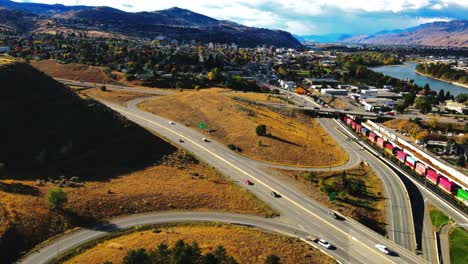 dolly-in-drone-shot-hyperlapse-of-Kamloops-BC-Canada-with-Bridges,-the-Highway-1-and-Yellowhead-Highway-5-on-a-sunny-day-in-the-desert-city-with-cars,semi-trucks-and-trains-driving-in-the-foreground