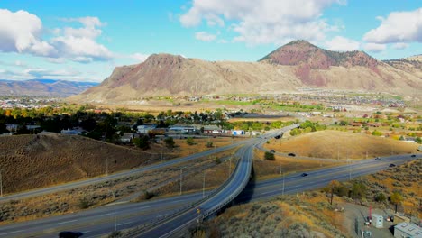dolly-in-drone-shot-of-Bridges-and-the-Highway-1-and-Yellowhead-Highway-5-in-Kamloops-BC-Canada-,-on-a-Cloudy-Day-in-a-desert-city-with-cars-and-semi-trucks-driving-and-mount-paul-in-the-background