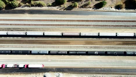 bird's-eye-view-truck-sideways-drone-shot-flying-over-railroad-station-in-a-desert-environment-on-a-sunny-day-with-cargo-and-tank-tain