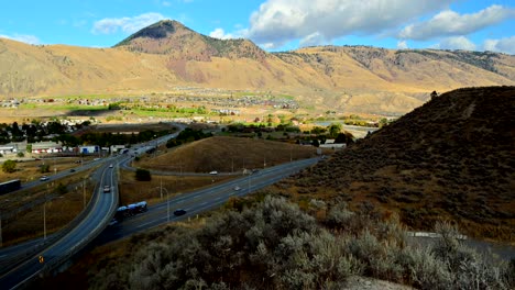 pan-right-shot-hyperlapse-of-Bridges-on-Highway-1-and-Yellowhead-Highway-5-in-Kamloops-BC-Canada-,-with-cars-and-semi-trucks-driving,-mount-paul-in-the-background-and-desert-vegetation-in-front