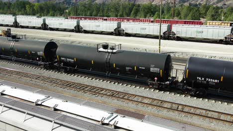 sideview-dolly-forward-drone-shot-flying-over-railroad-station-in-a-desert-environment-on-a-sunny-day-over-black-tank-trains-and-other-cargo-trailers