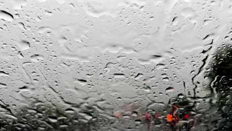 Raindrops-on-windscreen-and-red-blurred-lights-of-car-traffic-in-background,-wiper-cleaning-windshield-from-pouring-rain