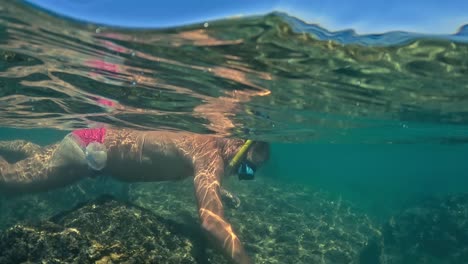 Half-underwater-view-of-man-with-mask-and-snorkel-fishing-sea-urchin-in-shallow-water