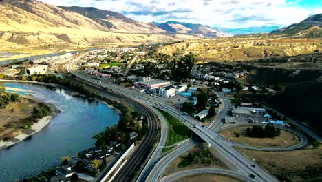 hyper-lapse-dolly-in-drone-shot-of-Bridges-and-the-Highway-1-and-Yellowhead-Highway-in-Kamloops-BC-Canada-with-train-trucks,-the-Thompson-River-on-a-Cloudy-Day-in-a-desert-environment