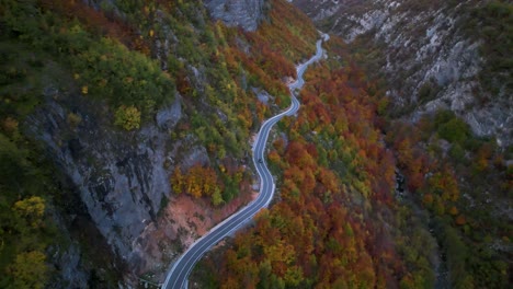Panoramic-winding-road-alongside-mountain-slope-covered-by-colorful-forest-in-autumn