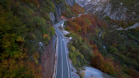 Road-winds-along-the-mountainside-covered-by-trees-with-colorful-leaves-in-autumn,-Albanian-Alps