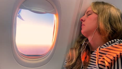 Woman-Sleeping-on-Plane-During-Golden-Hour,-Listening-to-Music-on-Airplane
