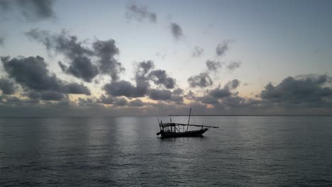 Fishing-boat-floating-near-Uroa-beach-coastline-in-Zanzibar-Island,-Tanzania-Africa-during-sunset,-Aerial-orbit-around-shot