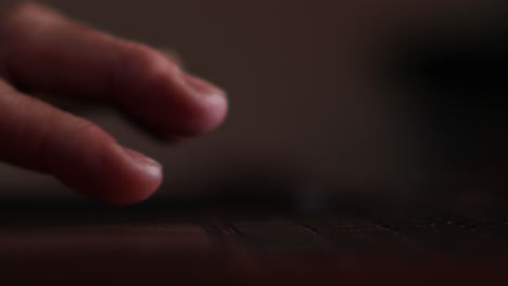 Close-up-of-man's-fingers-scrolling-and-tapping-the-track-pad-of-a-laptop-backlit-by-the-screen