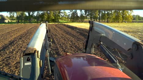 Flock-of-birds-rise-from-freshly-cultivated-field-as-farmer-drives-a-tractor,-view-from-cabin