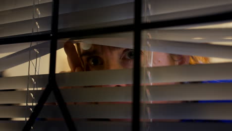 A-paranoid-scared-woman-looking-through-blinds-at-home