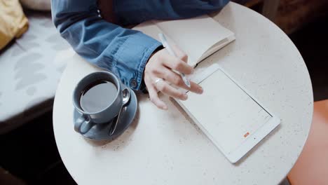 Person-Sieht-Sich-Einen-Digitalen-Terminplaner-An,-Während-Sie-Mit-Einer-Kaffeetasse-Am-Tisch-Sitzt