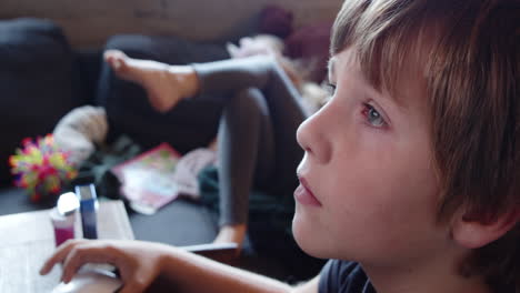 Close-up-of-the-face-of-a-boy-sitting-concentrated-in-front-of-a-computer-and-a-girl-on-a-couch-who-is-bored