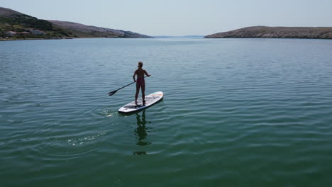 aerial-landscape-of-sunny-summer-day-with-silhouette-of-a-girl-paddling-on-Adriatic-sea-of-Pag-Island-in-Croatia
