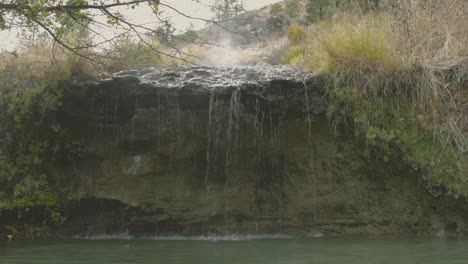 Hot-spring-waterfall-with-steam-rising-up-from-hot-pool-in-Boise-National-Forest-Idaho-Static-shot-then-rises-to-sky