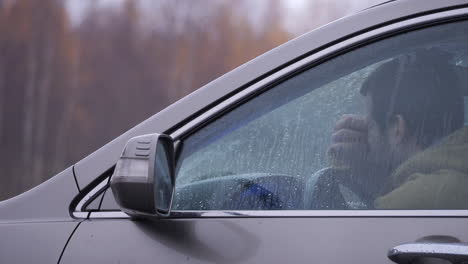 Tired-driver-yawns,-tries-to-stay-awake-and-starts-car,-autumn-rain-daytime