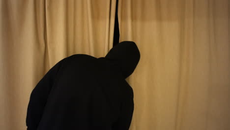 A-man-in-a-black-hood-is-suspicious-and-in-opening-the-curtains-to-spy-outside