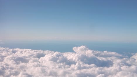 Motion-shot-from-the-window-of-an-airplane-with-fluffy-clouds-beneath-and-a-blue-sky-above