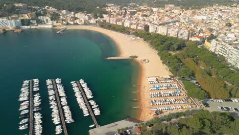 Aerial-images-of-Sant-Feliu-de-Guixols-on-the-Costa-Brava-of-Girona-small-boats-on-the-yellow-sand-beach-and-turquoise-blue-water-of-the-Mediterranean