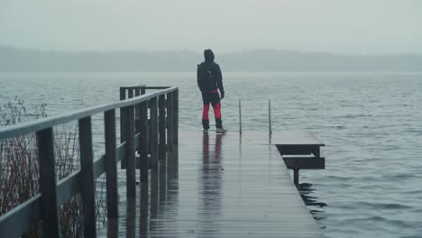 Man-walking-on-a-wet-pier-and-looking-towards-the-lake-on-a-cold-and-rainy-day