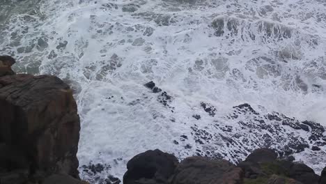 Waves-swell-and-crash-against-the-rocks,-high-angle