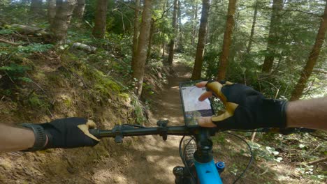 Man-stops-on-trail-while-mountain-biking-to-see-where-he-is-at-using-phone-mounted-to-bike-for-navigating-next-moves