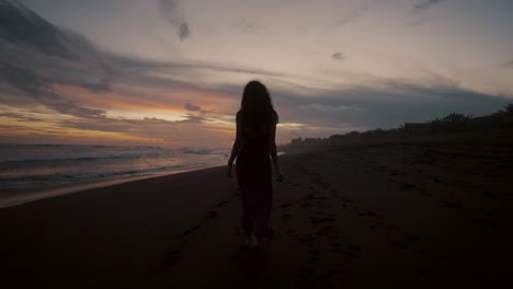 A-Woman-Walking-Alone-On-The-Shore-During-Sunset-In-Summertime