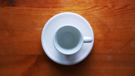 Top-shot-of-an-ampty-espresso-cup-standing-on-a-white-plate-on-a-brown-wooden-Table