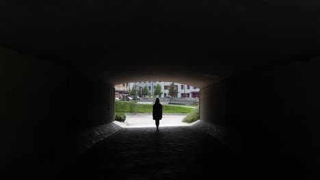 Silueta-Mujer-Caminando-En-Un-Túnel-Oscuro-Saliendo-Del-Paso-Subterráneo-A-La-Calle-Brillante-En-Letonia,-Vista-Trasera