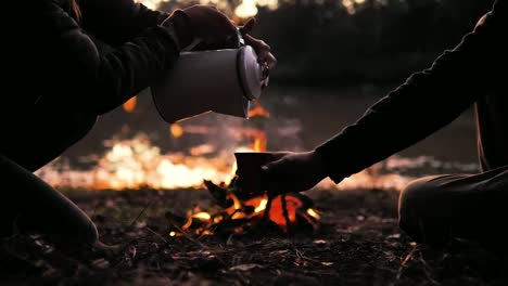 Camping-in-the-forest-pouring-hot-water-in-the-cup-in-front-of-the-fireplace-in-the-evening