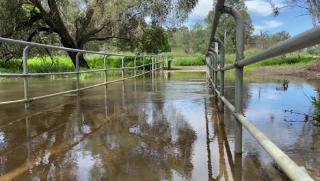 Low-angle-looking-across-a-flooded-foot-bridge-over-a-swollen-creek-following-flooding-rain-and-inundation-in-the-Australian-Floods-in-October-2024