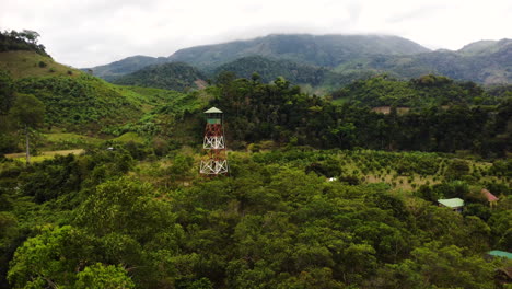 Aerial-circling-observation-tower-among-lush-vegetation,-near-countryside,-Vietnam