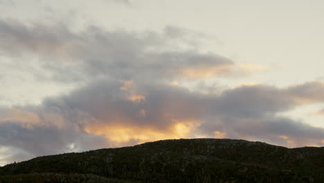 Wolken,-Die-Bei-Sonnenuntergang-Langsam-über-Dem-Berggipfel-Vorbeiziehen,-Gelb-Gefärbt-Von-Der-Untergehenden-Sonne