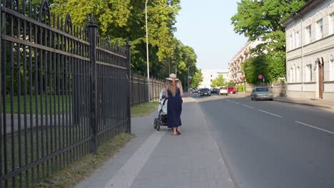Elegante-Mujer-Caucásica-Empujando-Un-Cochecito-De-Bebé-En-La-Calle-Cerca-Del-Parque,-Letonia