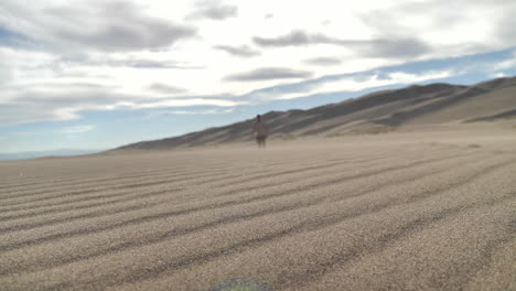 Wide-Cinematic-Shot-of-Sand-Blowing-While-Blurred-Traveler-Approaches