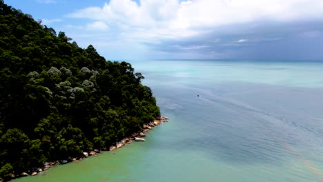 Aerial-drone-backing-up-shot-of-blue-sea-and-dense-trees-forest-along-the-island-in-Penang-National-Park,-Penang,-Malaysia-at-daytime