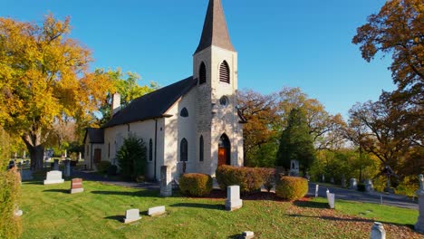 Tieffliegende-Drohne-über-Ländlichem-Friedhof-Mit-Kleiner-Landkirche-Und-Herbstbäumen