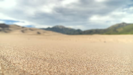 Close-Up-Sand-Grains-in-Desert-with-Mountain-Range-Background