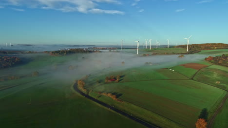 Aerial-drone-forward-moving-shot-of-green-farmlands-and-windmills-in-Gabsheim,-Rhineland-Palatinate,-Germany-on-a-foggy-morning